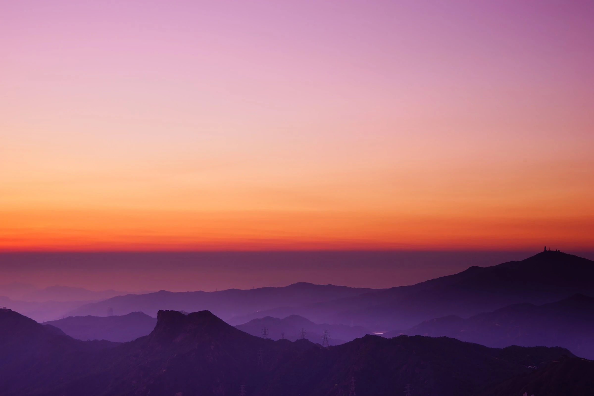 Layered mountain ridges at sunset under a pink and orange sky